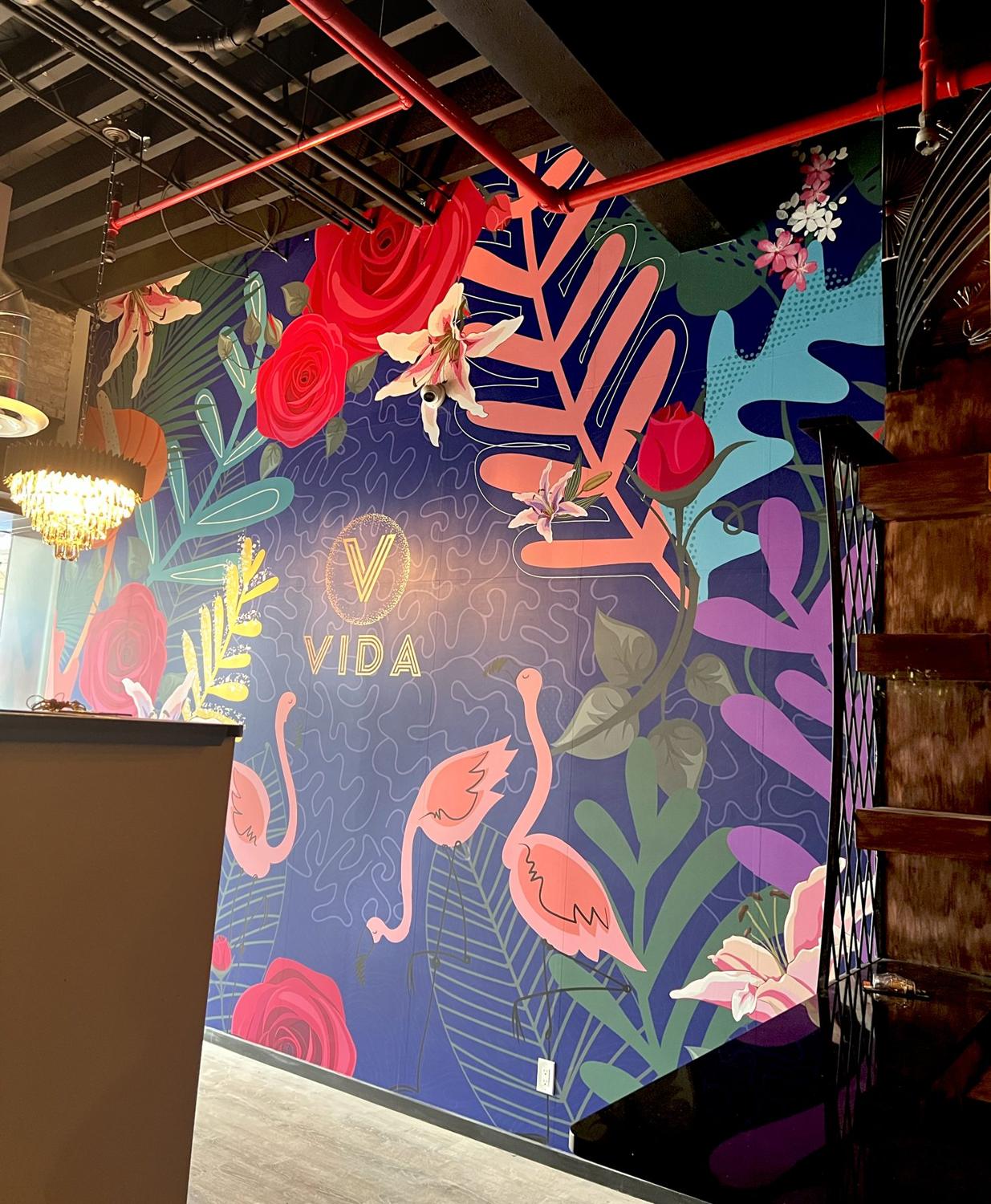 Tropical floral wall with flamingos and gold VIDA logo in a restaurant