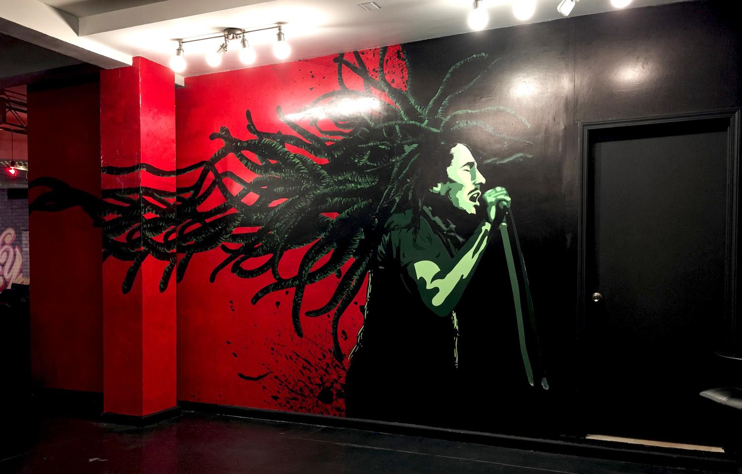 Red and black mural of a singer with flowing locs wrapping a column and wall